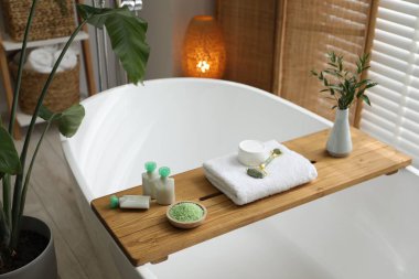 Spa ürünleri ve banyo küvetinde yeşil dalları olan ahşap tepsi.