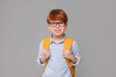 Gri arka planda sırt çantası olan mutlu okul çocuğu.