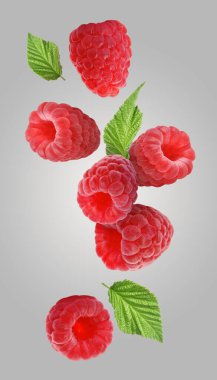 Taze olgun ahududu ve yeşil yapraklar gri arka plana dökülüyor.