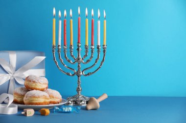 Hanuka kutlaması. Yanan mumlar, dreideller, çörekler ve açık mavi masa üzerinde hediye kutusu olan Menorah, metin için yer
