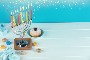 Hanuka kutlaması. Menorah yanan mumlar, dreidels, hediye kutuları ve beyaz ahşap masa üzerinde donut, metin için yer