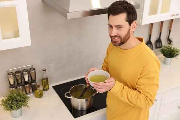 Man with bowl of delicious soup in kitchen