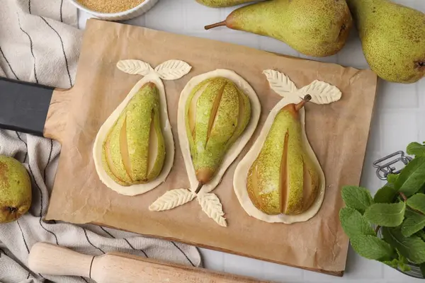 stock image Board with raw dough, fresh pears and mint on white tiled table, flat lay