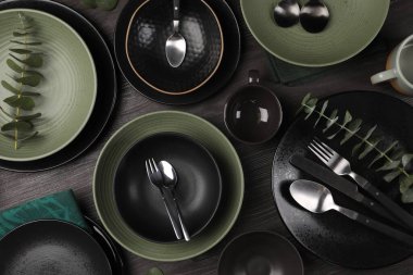 Koyu ahşap zemin üzerinde çatal bıçak ve okaliptüs dallarıyla süslü masa seti.