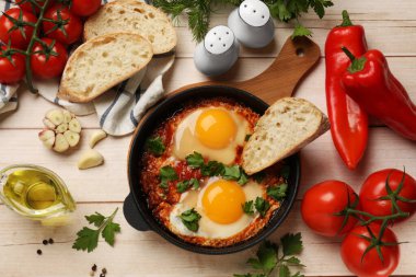 Düz kompozisyon ve lezzetli Shakshuka hafif ahşap masada kızartma tavasında
