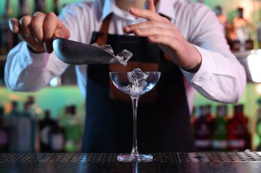 Alkolik kokteyl yapmak. Barmen, barda tezgahta Martini bardağına buz küpleri ekliyor.