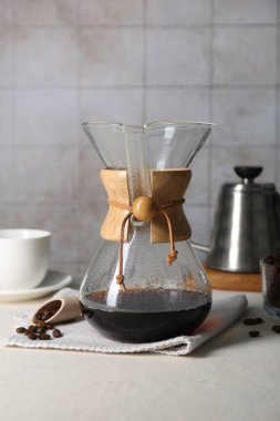 Glass chemex coffeemaker with tasty drip coffee and beans on white table clipart