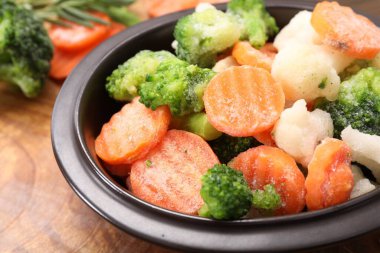 Tahta masadaki kasede farklı donmuş sebzelerin karışımı, yakın plan.