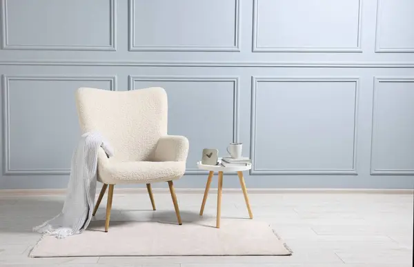 Comfortable armchair with blanket and side table indoors, space for text