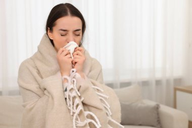Battaniyeye sarılı hasta bir kadın, evde burnunu siliyor, mesaj için yer var. Soğuk belirtileri