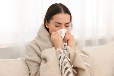 Hasta kadın battaniyeye sarılmış, evinde kanepede burnunu siliyor. Soğuk belirtileri