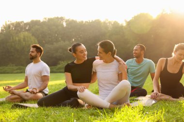 Kadınlar dışarıda minderlerde yoga yaparken birlikte vakit geçiriyorlar.