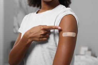 Kapalı alanda aşılandıktan sonra yapıştırıcı bandaja bakan genç bir kadın.