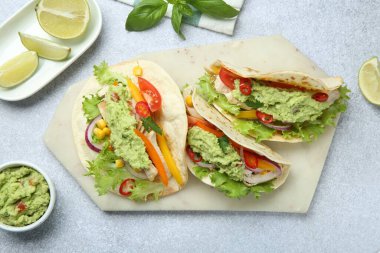 Guacamole soslu lezzetli tacolar, açık gri masada et ve sebzeler, düz uzanma