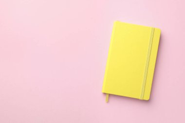 Açık pembe arka planda kapalı sarı defter, üst manzara. Metin için boşluk