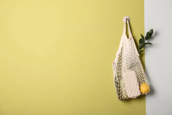 Conscious consumption. Net bag with eco friendly products hanging on olive wall, space for text
