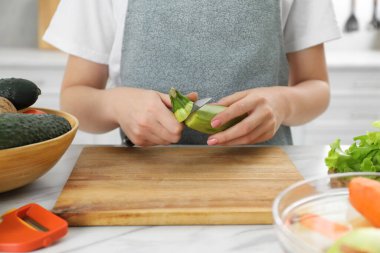 Kadın mutfaktaki beyaz mermer masada bıçakla kabak soyuyor, yakın plan.