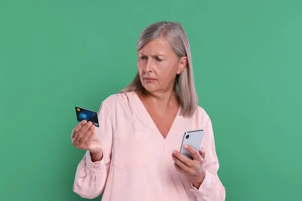 Worried woman with credit card and smartphone on green background. Be careful - fraud