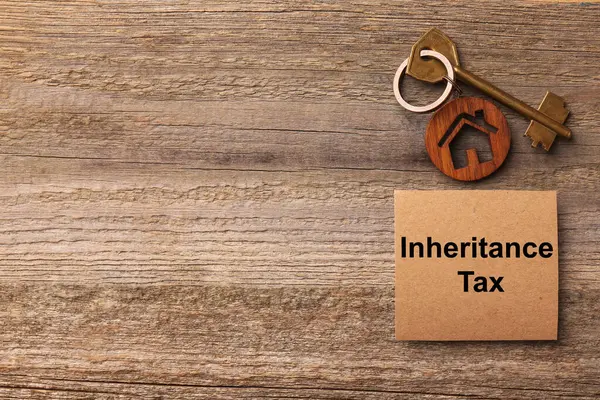 Inheritance Tax. Card and key with key chain in shape of house on wooden table, flat lay. Space for text
