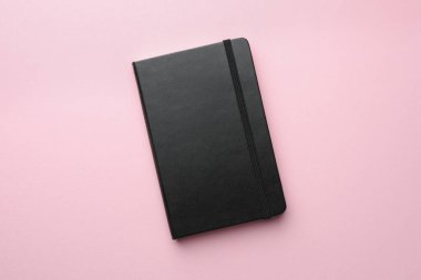 Açık pembe arka planda kapalı siyah defter, üst görünüm