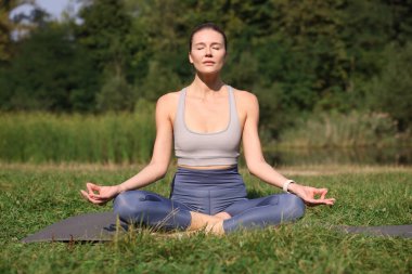 Güzel bir kadın dışarıda yoga yapıyor. Lotus pozu