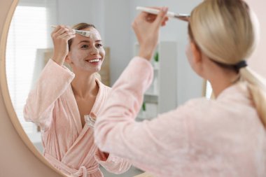 Banyoda aynanın yanında yüz maskesi takan bir kadın. Spa tedavileri
