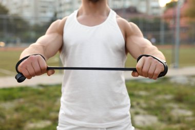 Kaslı adam dışarıda elastik direnç bandıyla egzersiz yapıyor, yakın plan.