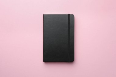 Açık pembe arka planda kapalı siyah defter, üst görünüm