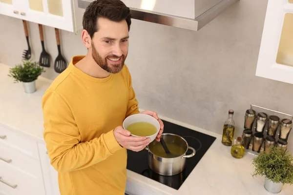 Man with bowl of delicious soup in kitchen
