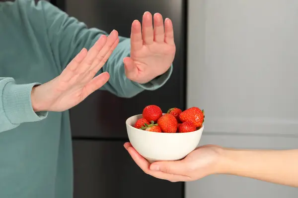 Woman suffering from food allergies refusing offered strawberries by her friend at home, closeup