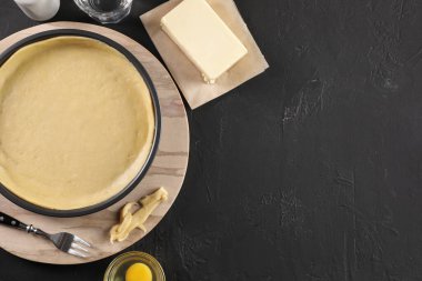 Kiş yapıyorum. Taze hamurlu turta tenekesi ve malzemeler siyah masada, düz yerde. Metin için boşluk