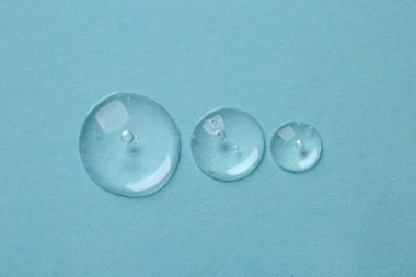 Açık mavi arkaplanda kozmetik serumu damlaları, üst görünüm