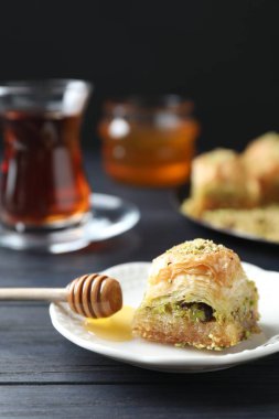 Lezzetli taze baklava ve siyah ahşap masada doğranmış fındıklı bal, yakın plan. Doğu tatlıları