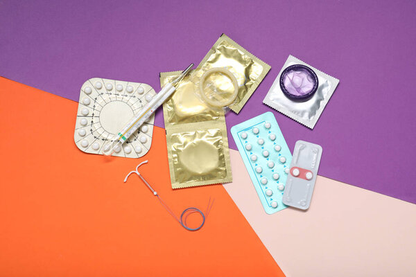 Противозачаточные таблетки, презервативы, внутриутробное устройство и термометр на цветном фоне, плоский уголок. Выбор метода контрацепции