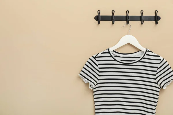 Hanger with striped t-shirt on beige wall, space for text