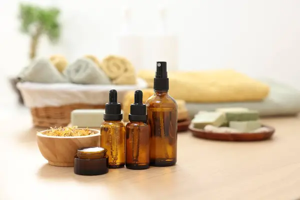 Bottles of essential oils, dry flowers and jar with cream on light wooden table, space for text. Spa therapy