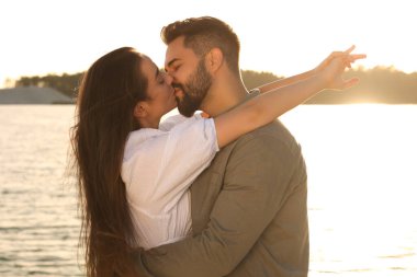 Happy couple kissing near river on sunny day clipart