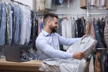 Kuru temizleme servisi. Kapalı mekanda naylon torba içinde askı tutan mutlu işçi.
