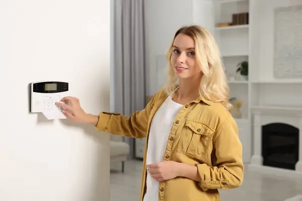 Woman entering code on home security system in room