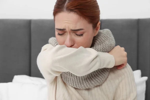 Woman with scarf coughing on bed. Cold symptoms