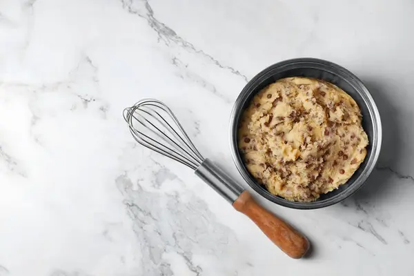 Stock image Chocolate chip cookie dough in bowl and whisk on white marble table, flat lay. Space for text