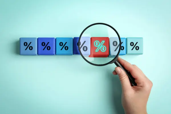Best mortgage interest rate. Woman looking at red cube with percent sign through magnifying glass on cyan background, top view