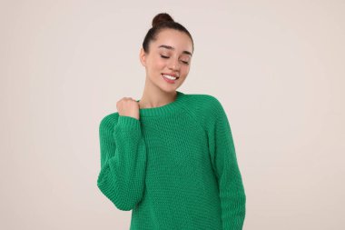 Açık gri arka planda, şık, sıcak süveter giyen güzel genç bir kadın.