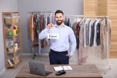Kuru temizleme servisi. Mutlu işçi işyerinde açık tabela tutuyor.