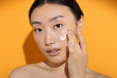 Güneş ışığı altında, yüzü turuncu arka planda güneş kremi sürmüş güzel genç bir kadın.