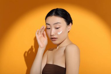 Güneş ışığı altında, yüzü turuncu arka planda güneş kremi sürmüş güzel genç bir kadın.