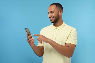 Açık mavi arka planda akıllı telefondan mesaj gönderen mutlu adam