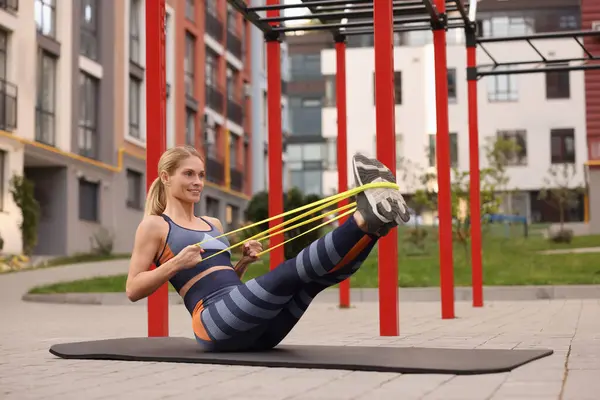 Athletic woman doing exercise with fitness elastic band on mat at outdoor gym