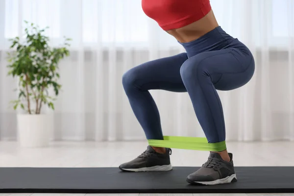 Woman doing squats with fitness elastic band on mat at home, closeup. Space for text