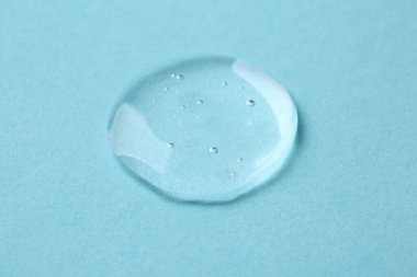 Açık mavi arkaplanda kozmetik serumu damlası, yakın plan